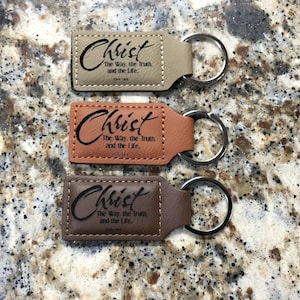 May include: Three brown leather keychains with silver key rings. Each keychain has the words "Christ The Way, the Truth, and the Life."  John 14:6.