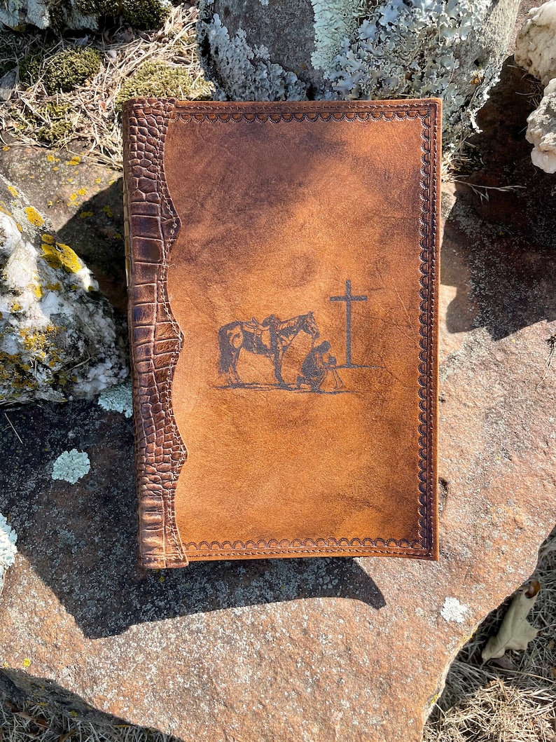 May include: A brown leather-bound journal with a decorative border and a tooled design of a horse and rider kneeling before a cross.
