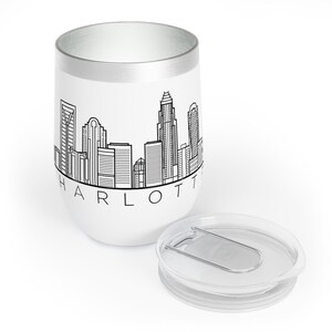May include: White stainless steel travel mug with a black outline of the Charlotte skyline and the word "CHARLOTTE" printed below. The mug has a clear lid with a silver slider.