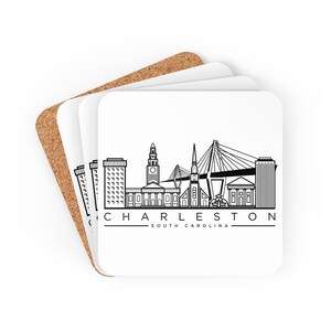 May include: White square coasters with a black and white line drawing of the Charleston, South Carolina skyline. The text "CHARLESTON SOUTH CAROLINA" is printed below the skyline. The coasters are stacked on top of a cork coaster.