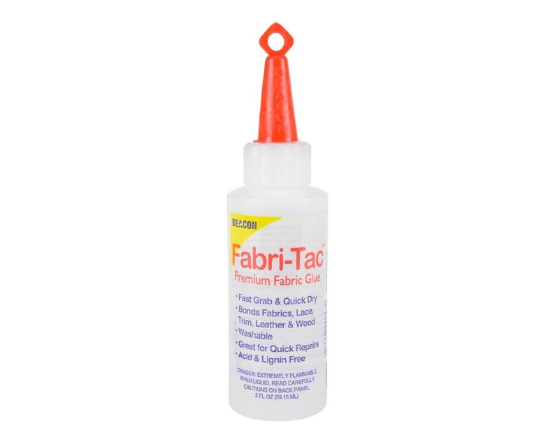 May include: A clear plastic bottle of Fabri-Tac Premium Fabric Glue with a red cap and a red applicator tip. The bottle is labeled with the product name and instructions for use. The bottle contains 2 fl oz (59 ml) of glue.