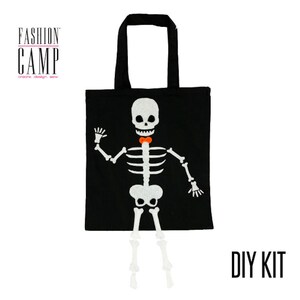 Peut inclure: Kit de bricolage pour un sac fourre-tout d'Halloween avec un squelette portant un n&oelig;ud papillon. Le sac fourre-tout est noir avec un motif de squelette blanc et le texte "FASHION CAMP create design sew" en haut. Le texte "DIY KIT" est imprim&eacute; en blanc sur fond noir.