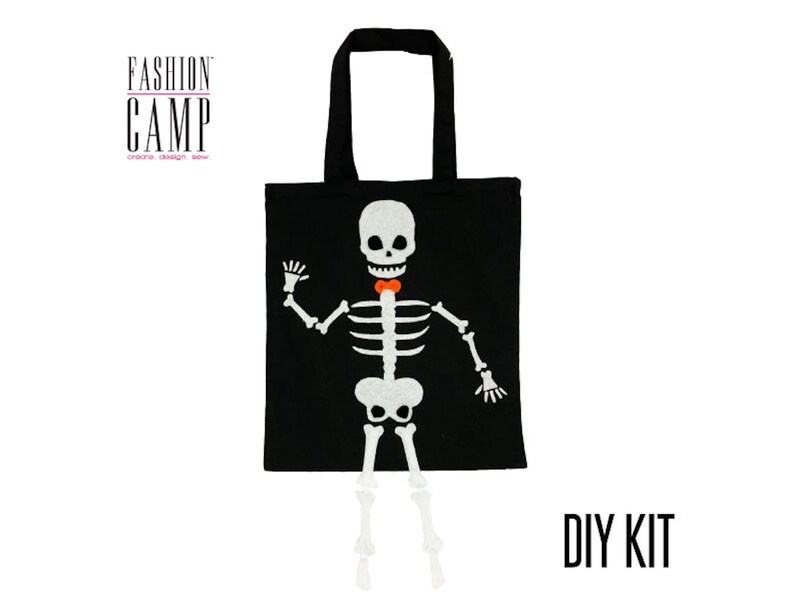 Peut inclure: Kit de bricolage pour un sac fourre-tout d'Halloween avec un squelette portant un n&oelig;ud papillon. Le sac fourre-tout est noir avec un motif de squelette blanc et le texte "FASHION CAMP create design sew" en haut. Le texte "DIY KIT" est imprim&eacute; en blanc sur fond noir.