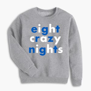 May include: A gray sweatshirt with the words "eight crazy nights" printed on the front in blue and white block letters. The sweatshirt has a crew neck and long sleeves.