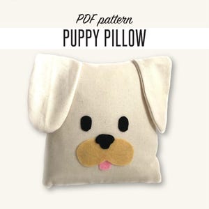 May include: A cream-colored puppy pillow with black eyes, a tan nose, and a pink tongue. The pillow has large, floppy ears and is labeled "PDF pattern PUPPY PILLOW" in black text. The Fashion Camp logo is in the upper left corner.