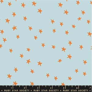 May include: Light blue fabric with a scattered pattern of orange stars. The fabric has a soft, matte finish. The text "RUBY STAR SOCIETY" is printed along the bottom edge. This fabric is suitable for quilting and sewing projects.