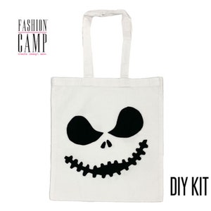 Peut inclure: Sac fourre-tout blanc avec un motif de visage de Jack Skellington noir. Le sac a des anses noires et le texte "FASHION CAMP create design sew" en rose. Le texte "DIY KIT" est en noir dans le coin inf&eacute;rieur droit du sac.
