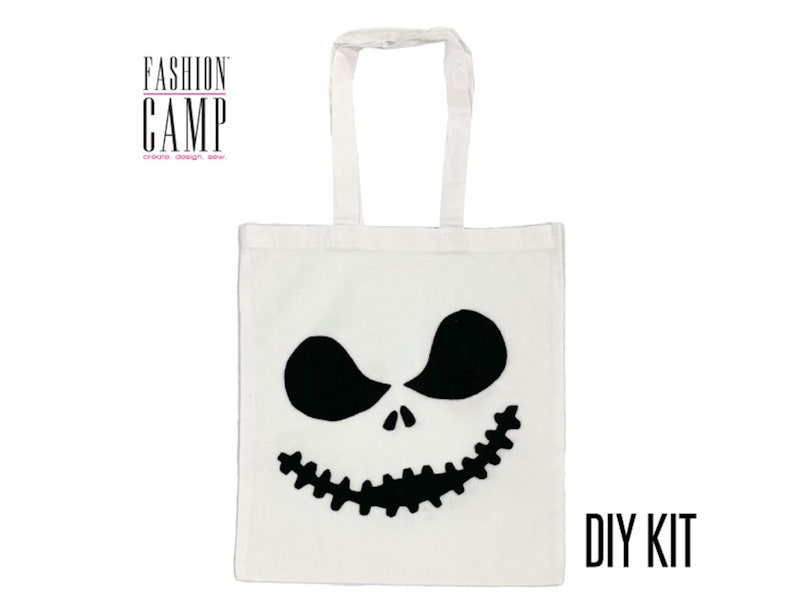 Peut inclure: Sac fourre-tout blanc avec un motif de visage de Jack Skellington noir. Le sac a des anses noires et le texte "FASHION CAMP create design sew" en rose. Le texte "DIY KIT" est en noir dans le coin inf&eacute;rieur droit du sac.