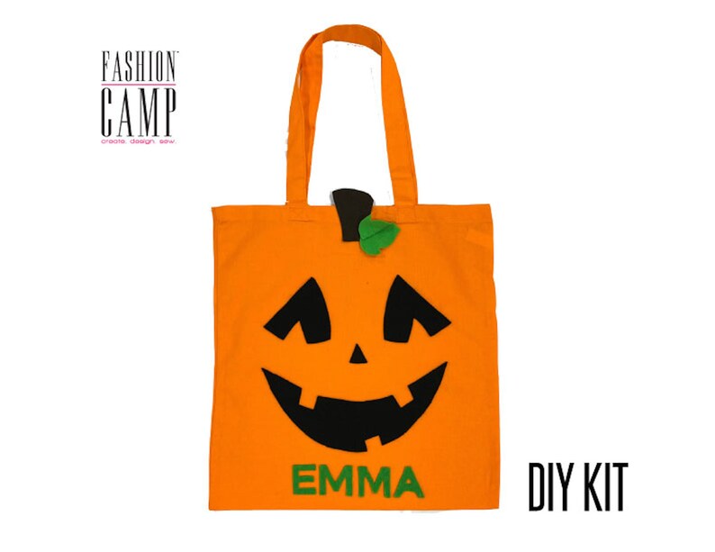 Peut inclure: Sac fourre-tout en tissu orange avec un visage de citrouille en feutre noir et une tige en feutre vert. Le sac porte l'inscription "FASHION CAMP" et "DIY KIT". Le nom "EMMA" est &eacute;crit en feutre vert sur le devant du sac.