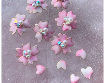May include: A set of 12 pink and white cherry blossom nail charms with gold accents and iridescent rhinestones. The charms are arranged on a white background. *12x12