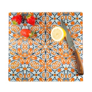 May include: A white and orange patterned glass cutting board with a lemon wedge, three strawberries, and a silver knife with a wooden handle.