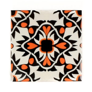 Op de afbeelding: Een vierkante keramische tegel met een geometrisch patroon in zwart en wit. Het patroon heeft oranje accenten en een centraal bloeiende ontwerp.
