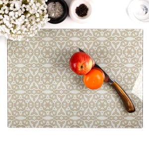 May include: A glass cutting board with a beige and white geometric pattern. The board has a knife and two pieces of fruit on it, one apple and one orange.