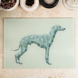 May include: A light green glass cutting board with a patterned silhouette of a greyhound dog.