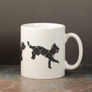May include: White ceramic mug with a black and white silhouette of a dog running. The dog is wearing a red collar. The dog is made up of a pattern of small black and white flowers.
