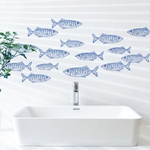 Op de afbeelding: Een witte wastafel met een chromen kraan bevindt zich onder een muur versierd met blauwe visstickers. De vissen zijn gestileerd met gedetailleerde patronen en gerangschikt in een zwemformatie, wat een nautisch thema aan de ruimte toevoegt.