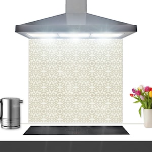 May include: A kitchen backsplash panel featuring a repeating geometric pattern in light beige and white. The rectangular panel is positioned behind a black induction cooktop and beneath a stainless steel range hood with integrated lighting.