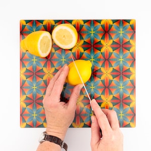 May include: A person's hands are shown cutting a lemon on a colorful cutting board with a geometric pattern. The cutting board has a blue, green, yellow, orange, and red pattern.