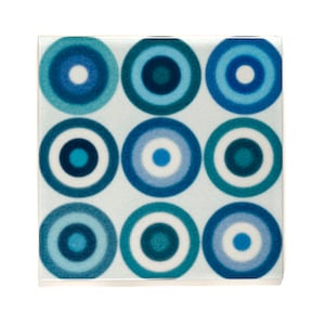 May include: A square tile featuring a blue and white concentric circle design. The tile has a light blue background with nine circles, each with a white centre and concentric rings of blue.