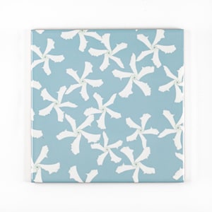 Può includere: Piastrella quadrata in ceramica con sfondo azzurro chiaro e un motivo ripetuto di forme floreali bianche stilizzate. I fiori hanno sei petali e un piccolo centro verde. Adatta per l'arredamento della casa.