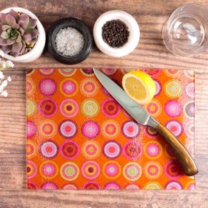 May include: A colourful glass chopping board with a retro pattern of pink, orange and yellow circles. A knife and a lemon wedge are on the board.