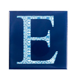 May include: Square, navy blue tile featuring the letter "E". The letter is filled with a white and light blue floral pattern. The tile has a glossy finish and is set against a white background.