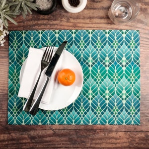 May include: A white plate with a fork, knife, and a napkin on a teal and green patterned placemat. A small orange sits on the plate.