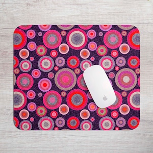 May include: A purple mouse mat with a repeating pattern of pink, red and white circles. A white computer mouse is on top of the mouse mat.