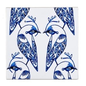 Puede incluir: Un azulejo de cerámica blanco con un patrón azul y blanco de pájaros estilizados. Los pájaros tienen diseños intrincados y se miran entre sí. El azulejo tiene un acabado brillante.