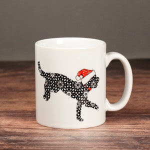 May include: White ceramic mug with a black and white patterned cat wearing a red Santa hat. The cat is in a walking pose.