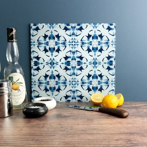 May include: A square glass cutting board with a blue and white floral pattern. The image also shows a bottle of liquor, lemons, a knife, and small bowls of salt and pepper on a wooden surface.