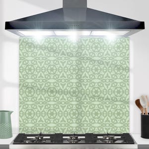 May include: A green and white patterned kitchen backsplash with a black range hood above it. The backsplash is made of tempered glass and is easy to clean.