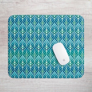 May include: A rectangular mouse mat featuring a teal and blue leaf pattern and a white wireless mouse. The mouse mat has a repeating design of stylized leaves in shades of teal, blue, and green. The mouse is a standard size.