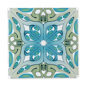 May include: A square tile featuring a blue, green and white geometric pattern. The pattern is symmetrical and has a star-like shape in the centre.