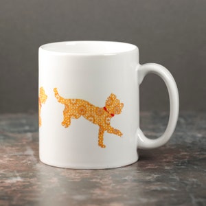May include: White ceramic mug featuring a yellow and orange floral design of a dog. The dog is wearing a red collar.