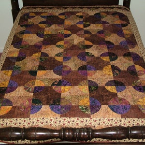 K&ouml;nnte beinhalten: Eine Steppdecke mit Patchwork-Muster aus braunem, violettem und goldenem Stoff. Die Steppdecke besteht aus Kreisen und Quadraten, und der Stoff hat ein Blumenmuster.