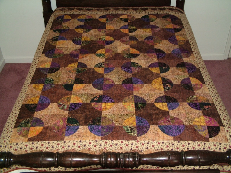 K&ouml;nnte beinhalten: Eine Steppdecke mit Patchwork-Muster aus braunem, violettem und goldenem Stoff. Die Steppdecke besteht aus Kreisen und Quadraten, und der Stoff hat ein Blumenmuster.