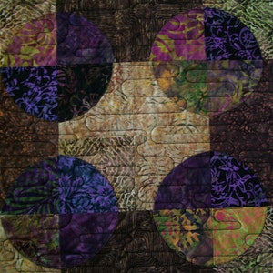 K&ouml;nnte beinhalten: Eine Steppdecke mit Patchwork-Muster, die Kreise in verschiedenen Schattierungen von Lila, Gr&uuml;n und Braun zeigt. Die Kreise sind in einem Gittermuster angeordnet und mit einem wellenf&ouml;rmigen Muster gesteppt.