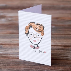 May include: A white card with a striped pattern features a hand-drawn illustration of a person with red hair wearing glasses and a pink collar. The text "Barb" is written below the illustration with a small red heart.