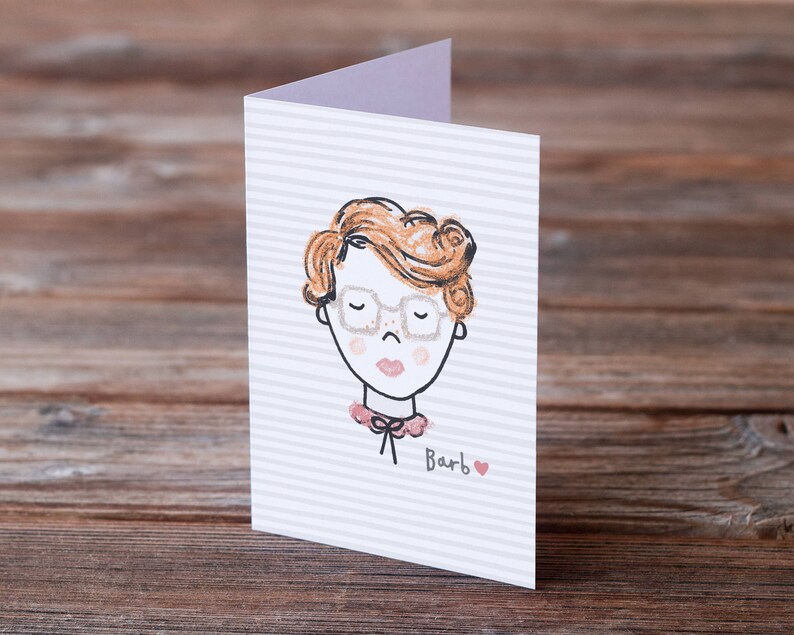 May include: A white card with a striped pattern features a hand-drawn illustration of a person with red hair wearing glasses and a pink collar. The text "Barb" is written below the illustration with a small red heart.