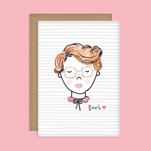 May include: A greeting card with a cartoon illustration of a person with red hair wearing glasses and a pink collar. The text "Barb" is written below the illustration with a small pink heart.