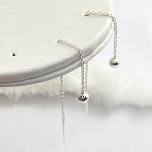 May include: A pair of silver dangle earrings with small round balls at the end of the chains.