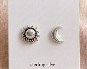 May include: A pair of sterling silver stud earrings. One earring is a sunburst design with a central sphere and surrounding beaded detail. The other earring is a crescent moon shape. The words "sterling silver" are printed below the earrings.