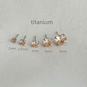 May include: A selection of titanium stud earrings, with sizes from 2mm to 5mm. Each earring features a light peach-colored gemstone. The word "titanium" is printed above the earrings.