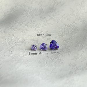 May include: Three heart-shaped purple gemstones, labelled 3mm, 4mm, and 5mm, are shown against a light background. The word "titanium" is above the gemstones. The gemstones are a deep violet colour.