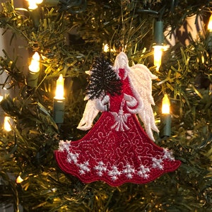 May include: Red and white angel Christmas ornament with a white halo and a black and white floral design. The ornament is hanging on a green Christmas tree with white lights.
