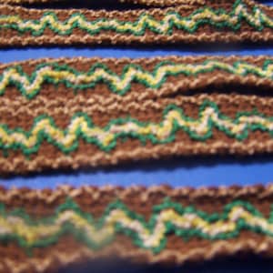 May include: Close-up of brown fabric trim with a zig-zag pattern of green, white, and yellow thread.