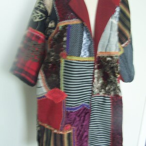 May include: A red, black, and white patchwork jacket with a long, open front. The jacket is made of different fabrics, including plaid, stripes, and floral patterns.