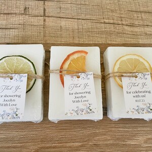 May include: Three white soap bars with dried citrus fruit on top. Each bar has a small thank you tag with a floral design and text that reads "Thank You for showering Jocelyn with Love" and "Thank You for celebrating with us! 10.17.25".