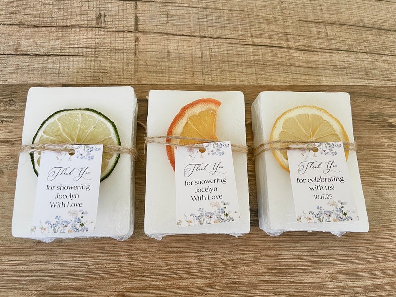 May include: Three white soap bars with dried citrus fruit on top. Each bar has a small thank you tag with a floral design and text that reads "Thank You for showering Jocelyn with Love" and "Thank You for celebrating with us! 10.17.25".